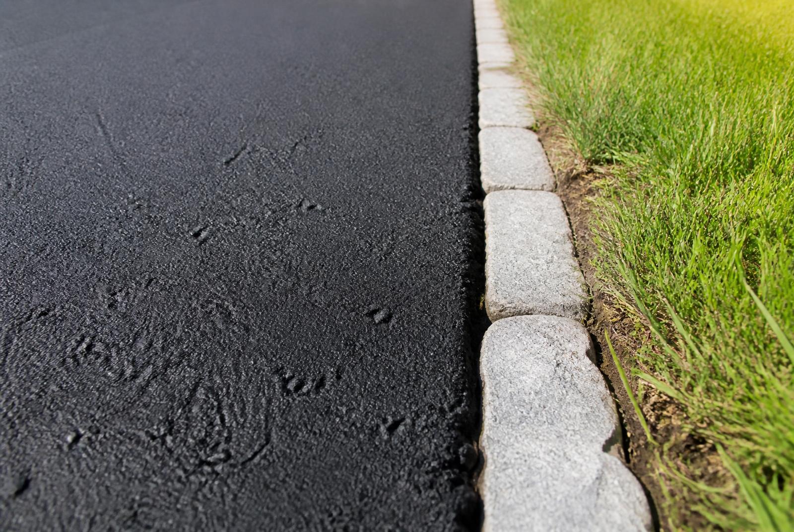 Close-up of a sealcoated asphalt driveway edge with granite block border
